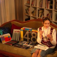 a woman sitting on a couch with books and other items in front of her,