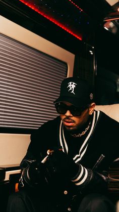 a man sitting on a train looking at his cell phone while wearing a hat and sunglasses