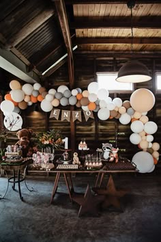 a table topped with lots of white and orange balloons next to a wooden ceiling filled with stars