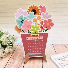 a desk calendar with flowers in it sitting on a wooden table next to a keyboard