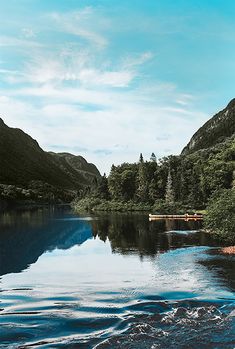 a lake surrounded by trees and mountains under a blue sky