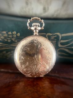 This pocket watch is in excellent antique condition. The gold fill is entirely intact and the watch runs perfectly. There are minor surface scratches indicative of age. The front of this piece is covered in stunning engravings and has the letter "A" at the bottom. The back mirrors the front in design but does not have the A.  The back panel opens to reveal the name Anna Bowman and the year 1911. The back panel does occasionally pop open a little but doesn't effect wear.  It weighs 37.4 grams and Victorian Engraved Gold Watches, Victorian Yellow Gold Pocket Watch For Anniversary, Heirloom Engraved Yellow Gold Pocket Watch, Antique 14k Stamped Watches, Antique 14k Stamped Round Watches, Gold Victorian Style Pocket Watch For Formal Occasions, Formal Yellow Gold Pocket Watch With Locket, Victorian Yellow Gold Pocket Watch Collectible, Victorian Yellow Gold Pocket Watch For Collectors