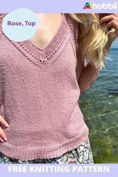 a woman standing next to the ocean with her hands on her hips, wearing a pink knitted top