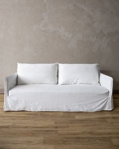 a white couch sitting on top of a hard wood floor next to a gray wall