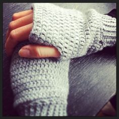 a person's hand holding onto a gray knitted mitt on top of a wooden table