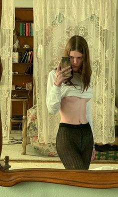 a woman taking a selfie in front of a mirror with her cell phone up to her chest