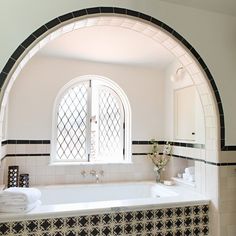 a bathroom with an arched window and black and white tiles on the walls, along with a large bathtub