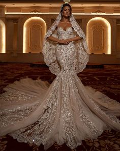 a woman in a wedding dress with an elaborate cape on her head and veil over her shoulders