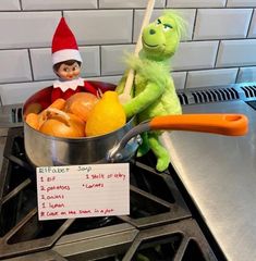 an elf is sitting on the stove with oranges in a pan next to him