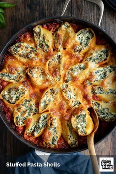 stuffed pasta shells with spinach and cheese in a skillet on a wooden table