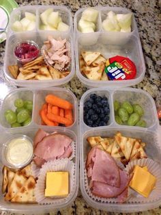 four plastic containers filled with food on top of a marble countertop covered in fruit and veggies