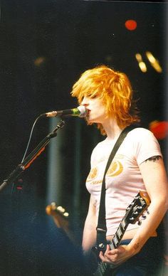 a woman with red hair is singing into a microphone and holding a guitar in her hand