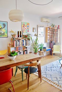 a dining room table with chairs and bookshelves in the background, surrounded by colorful furniture