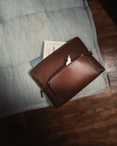 a brown briefcase sitting on top of a wooden floor next to a blue couch with pillows