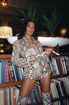 a woman standing in front of a bookshelf holding a snake skin print shirt