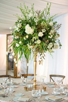 a tall vase filled with white flowers sitting on top of a table covered in plates and silverware