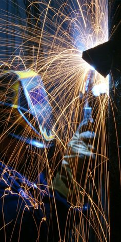 welders work on their laptops in the dark, with bright sparks coming from them