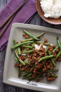 green beans with ground meat and rice on a plate next to chopsticks, fork and purple napkin