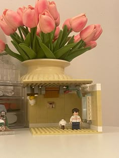 a vase filled with pink tulips sitting on top of a table next to a lego figure