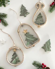 three christmas ornaments are hanging on a white surface next to evergreen branches and pine cones