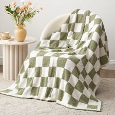 a green and white blanket sitting on top of a chair next to a vase with flowers