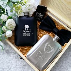 an open box containing two personalized flasks and a black bow tie with white flowers