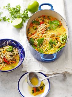 two bowls of food on a table with limes and spoons next to them