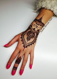 a woman's hand with henna tattoos on her left arm and pink nails