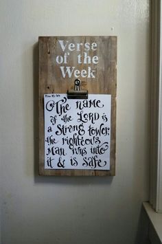 a wooden sign hanging on the side of a white wall next to a window with writing on it