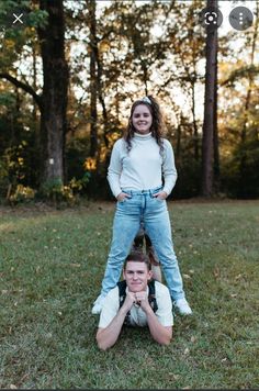 two people standing on one another in the grass with trees in the back ground behind them