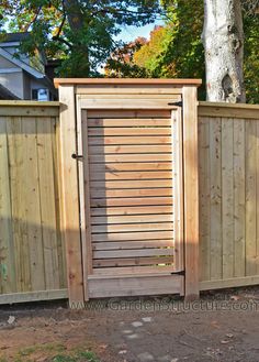 a wooden fence with an open door in the center and trees behind it, on a sunny day