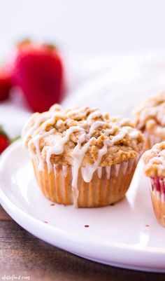 three strawberry muffins on a white plate with strawberries in the background