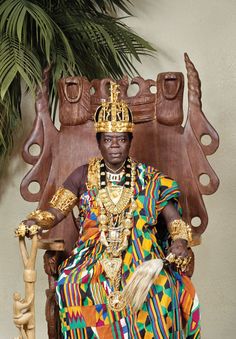 a statue of a man sitting on a chair with a cane in his hand and wearing an elaborate headdress