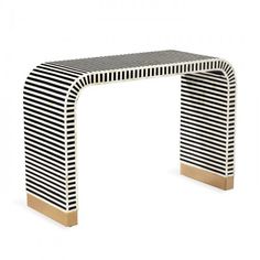 a black and white striped console table with gold trimmings on the top, in front of a white background