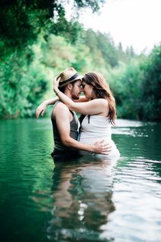 a man and woman are in the water hugging each other with trees in the background