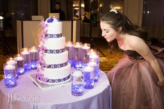 a woman in a purple dress looking at a wedding cake with lit candles on it