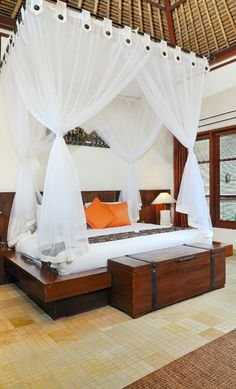 a bed with white drapes and orange pillows