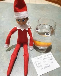 an elf is sitting on the table next to a jar of liquid and a note