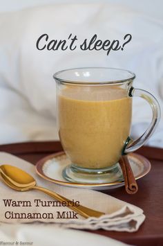 a glass cup filled with cinnamon milk sitting on top of a table next to a spoon