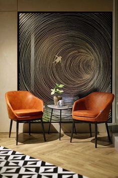 two orange chairs sitting next to each other in front of a black and white wall