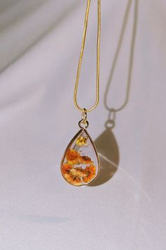 a gold necklace with an orange and white flower in the tear hanging from it's end