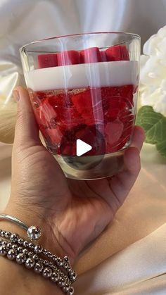 a person holding a glass filled with strawberries on top of a white table cloth