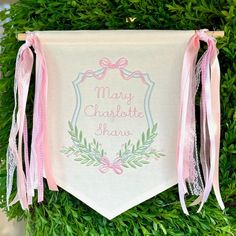 a white banner with pink ribbon hanging from it's side on top of a green bush