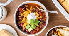 two bowls of chili with sour cream and tortilla bread on the side next to it