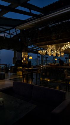 a dimly lit room with couches, tables and lamps on the ceiling at night