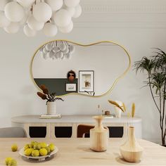 a dining room table with vases and fruit on it, in front of a large mirror