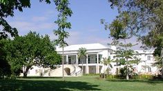 a large white house sitting in the middle of a lush green field next to trees