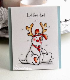 a card with a dog wearing reindeer antlers on it's head, sitting next to a cup