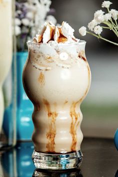 there is a drink with whipped cream in the glass on the table next to some flowers