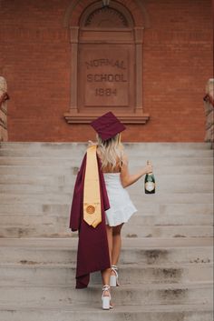 a woman in a graduation gown is holding a bottle of wine and standing on some steps